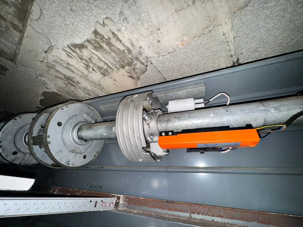 Eje completo de una puerta enrollable ya motorizado, con el motor naranja y el cableado recogido